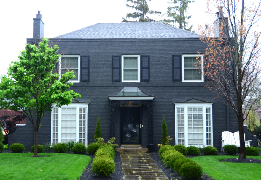 a brick home painted in dark grey with white windows